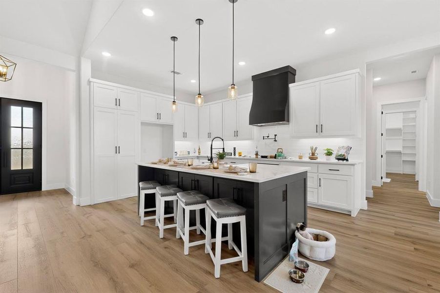 Kitchen with two tone color scheme, light wood-style floors, a kitchen bar, an island with sink, and light stone countertops