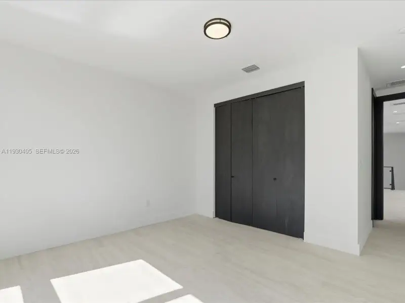 Interior space featuring wood-finish flooring, charcoal-toned bi-fold closet doors, and a central circular ceiling-mounted light fixture Interior space featuring wood-finish flooring, charcoal-toned bi-fold closet doors, and a central circular ceiling-mounted light fixture