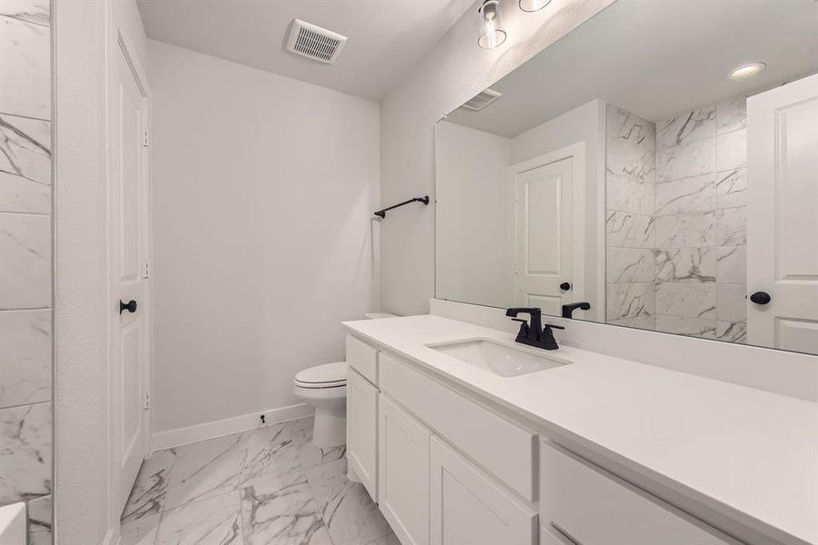 Bathroom with marble look tiles, vanity, baseboards, toilet, and recessed lighting