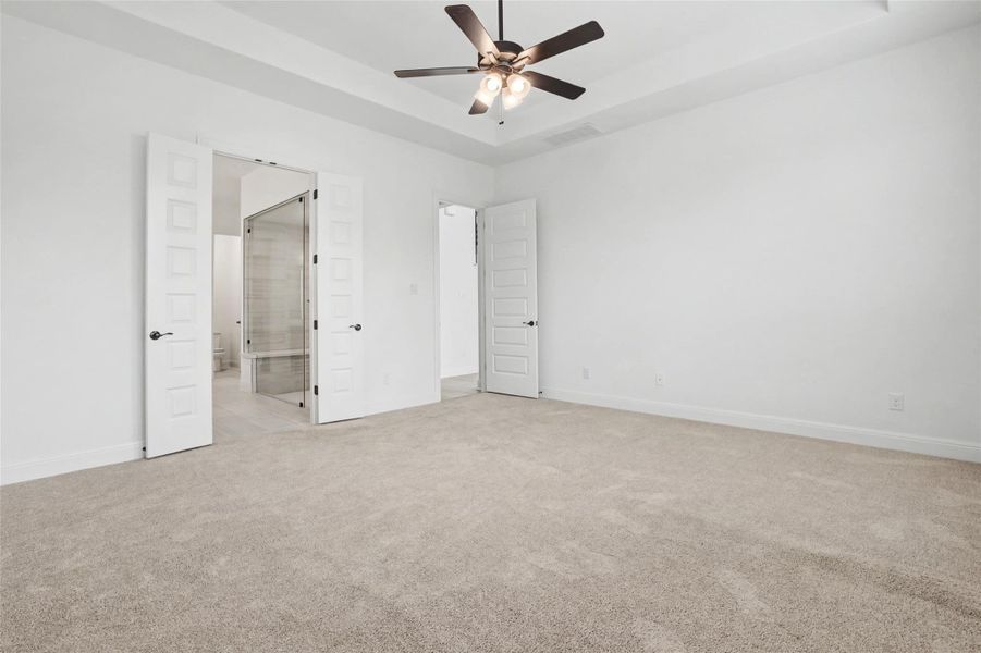 Unfurnished bedroom with light carpet, ensuite bath, a raised ceiling, and ceiling fan