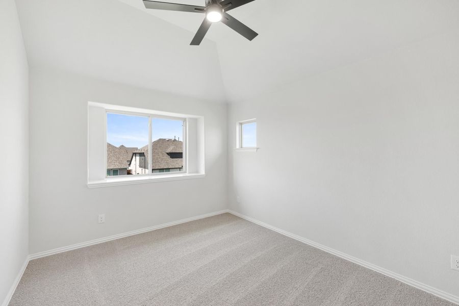 Empty bedroom with vaulted ceiling, ceiling fan, carpet flooring, and two windows Empty bedroom with vaulted ceiling, ceiling fan, carpet flooring, and two windows
