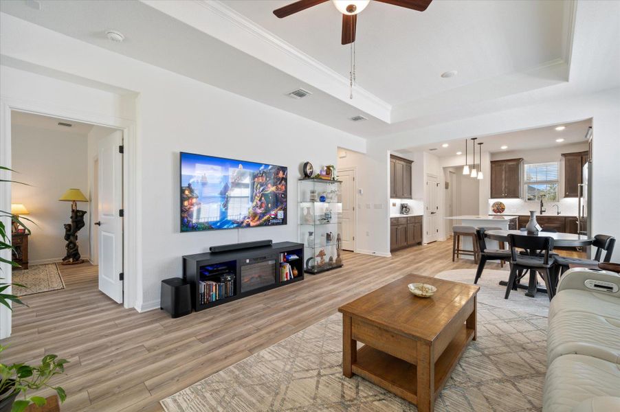 Living room with a ceiling fan, light wood-type flooring, a raised ceiling, ornamental molding, and recessed lighting Living room with a ceiling fan, light wood-type flooring, a raised ceiling, ornamental molding, and recessed lighting