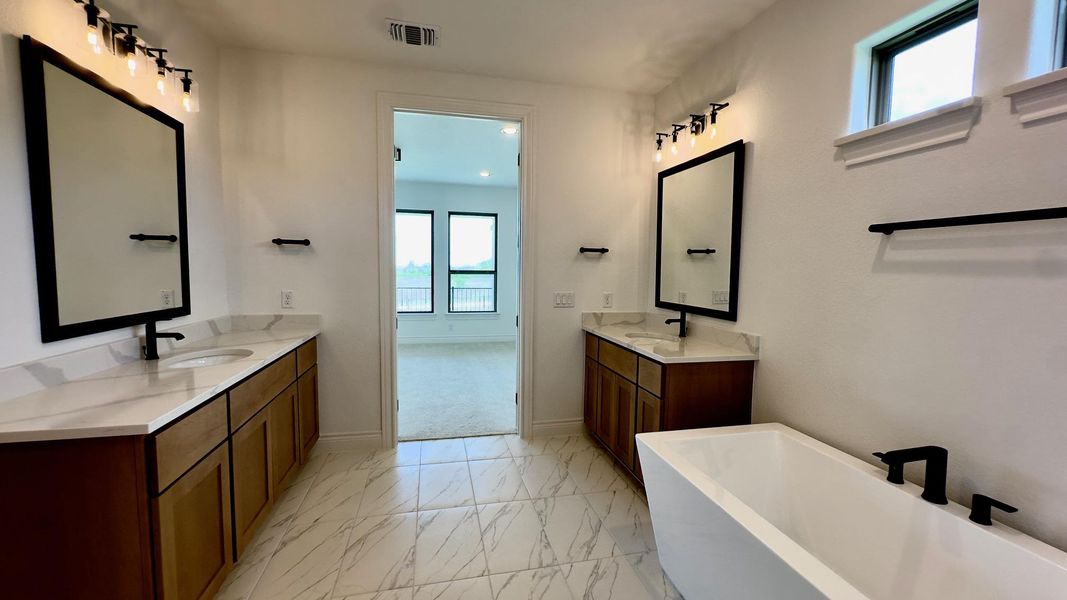 Full bath with two vanities, light marble finish flooring, and a soaking tub