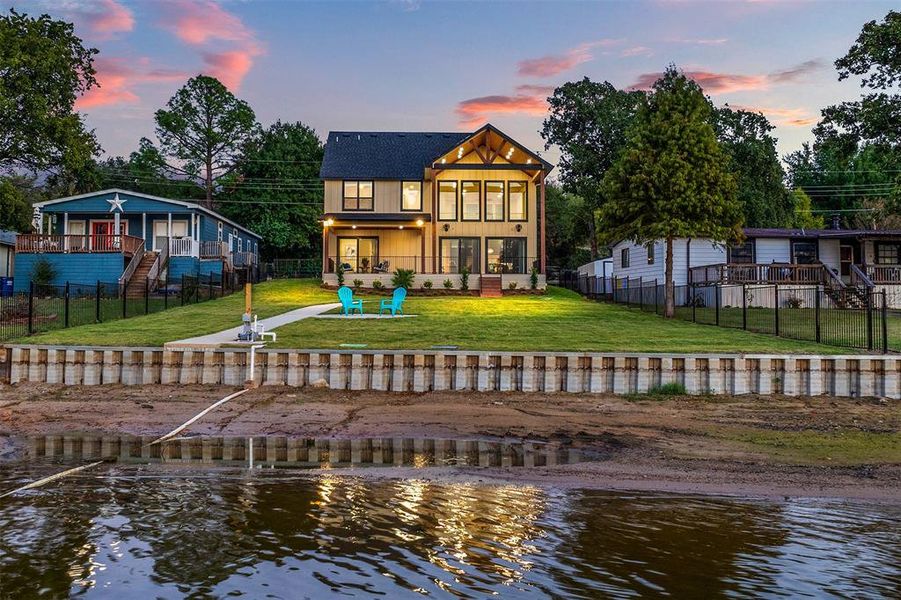 Back house at dusk featuring a lawn and a deck with water view