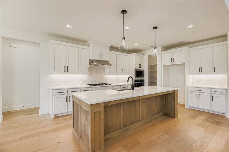 Kitchen with decorative backsplash, white cabinets, a kitchen island with sink, light wood finished floors, and recessed lighting Kitchen with decorative backsplash, white cabinets, a kitchen island with sink, light wood finished floors, and recessed lighting