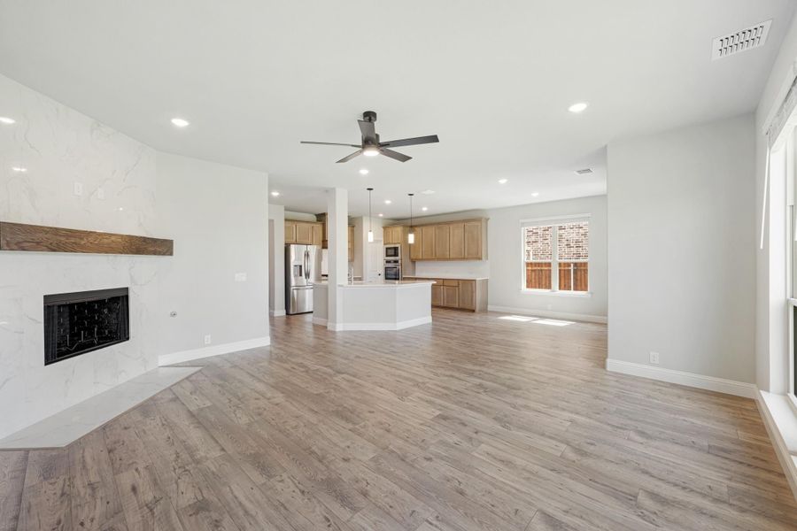 Open living area with marble fireplace, wood mantel, hardwood floors, and open kitchen with island beyond