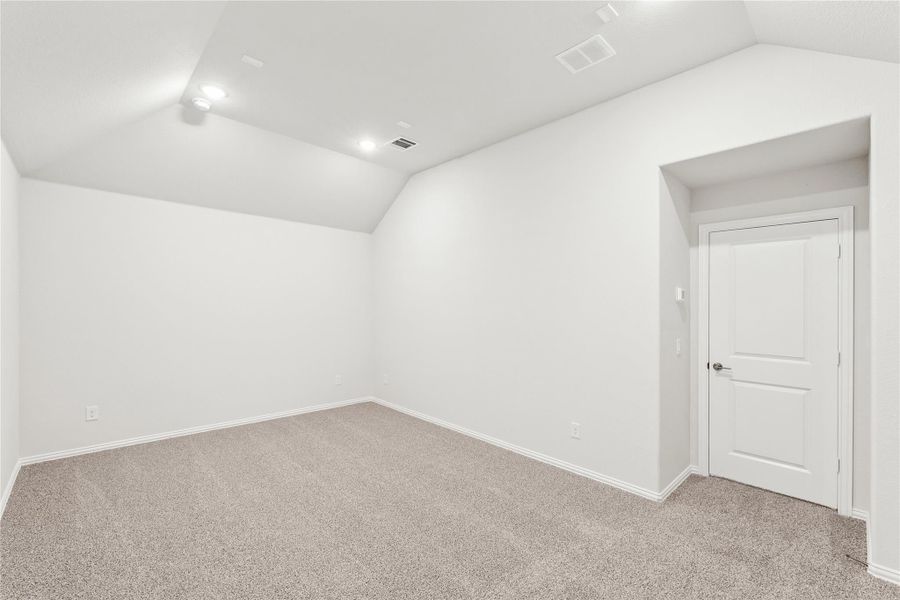Empty bedroom with vaulted ceiling, beige carpet, white walls, and a white paneled door
