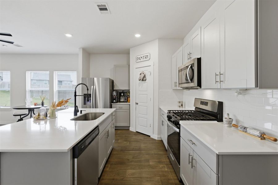 Kitchen with appliances with stainless steel finishes, dark wood-type flooring, a kitchen island with sink, decorative backsplash, and recessed lighting