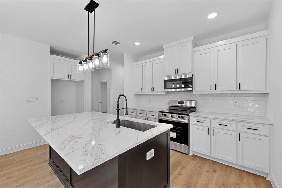 Kitchen featuring appliances with stainless steel finishes, a center island with sink, white cabinetry, light stone counters, and recessed lighting