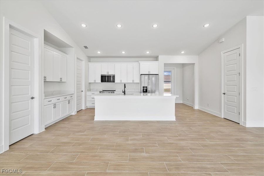 Kitchen with white cabinets, appliances with stainless steel finishes, a kitchen island with sink, recessed lighting, and wood tiled floors