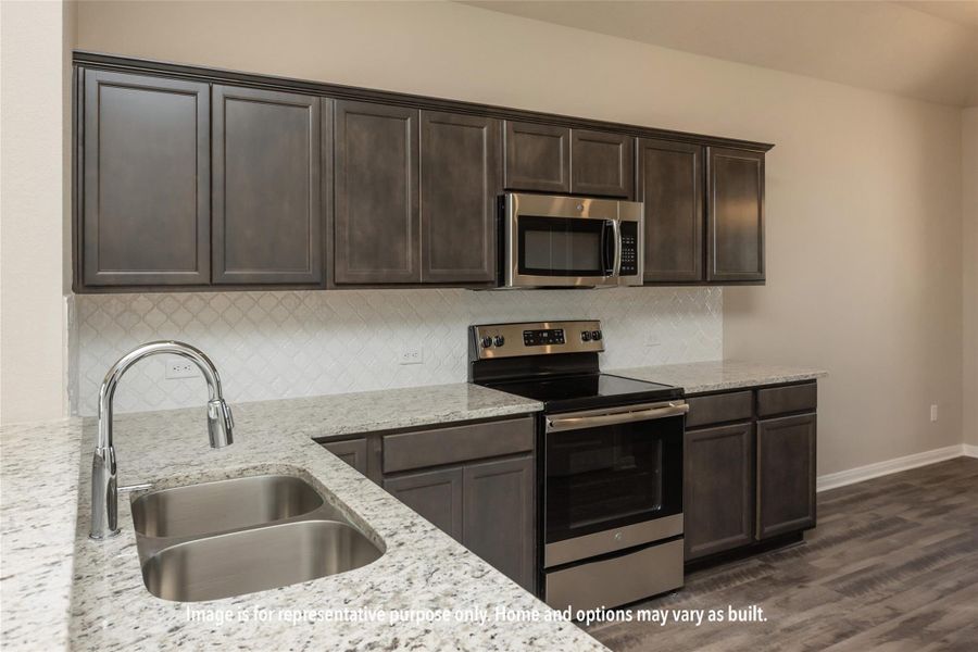 Kitchen featuring dark brown cabinets, stainless steel appliances, backsplash, light stone countertops, and dark wood-style flooring