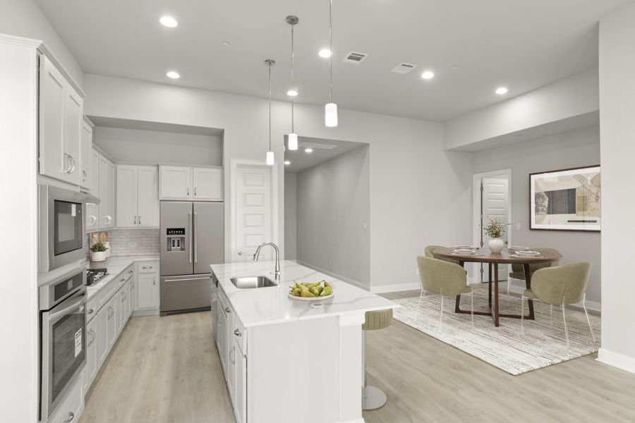 Image of a kitchen and dining room with a dining room rug and round table with dining setting, a stainless steel refrigerator and fruit set on the countertops