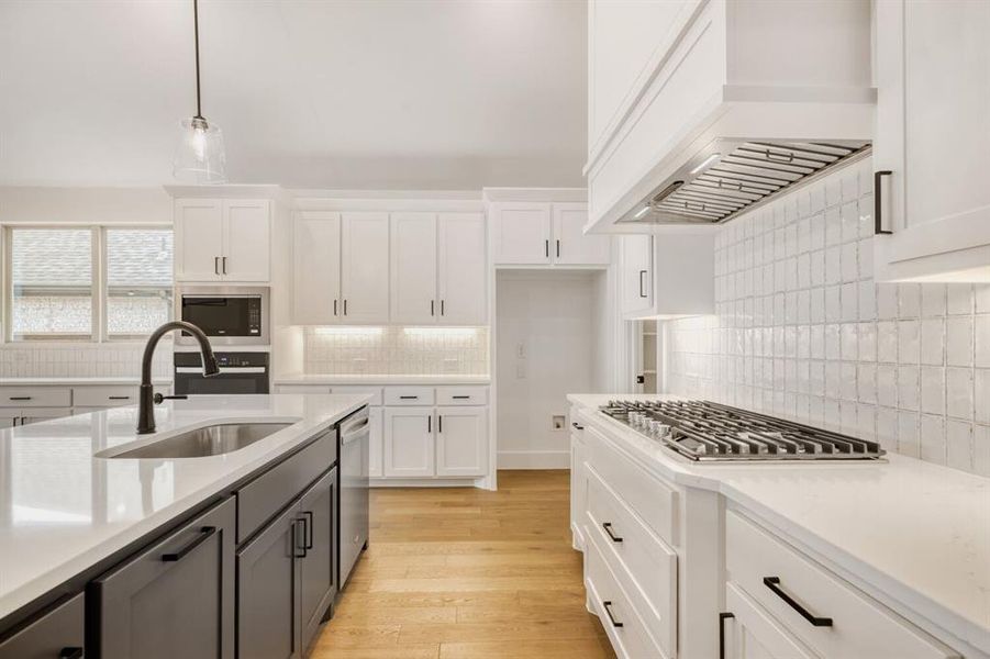 Two tone kitchen with light wood-style flooring, decorative light fixtures, dual tone cabinetry, stainless steel appliances, and backsplash