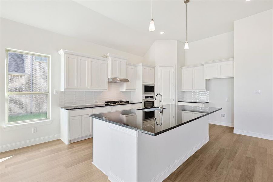 Kitchen with a kitchen island with sink, white cabinets, backsplash, and appliances with stainless steel finishes