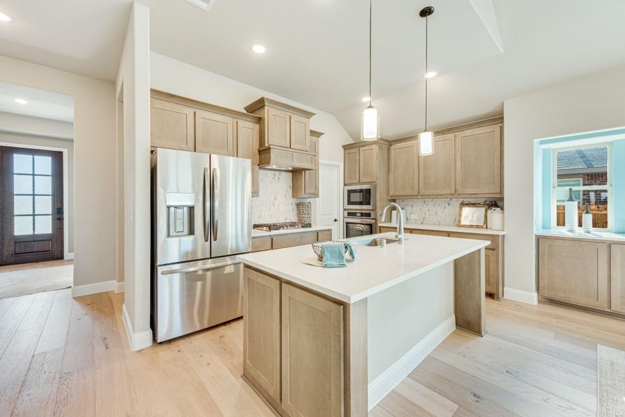 Kitchen with light wood cabinets, center island, stainless steel appliances, and hardwood floors