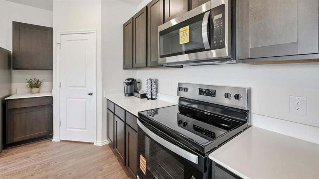Kitchen with stainless steel appliances, light wood-style flooring, and dark brown cabinetry Kitchen with stainless steel appliances, light wood-style flooring, and dark brown cabinetry