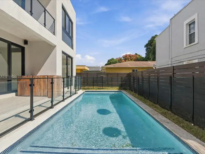Rectangular in-ground pool with tiled waterline, concrete patio, glass-panel railing, and horizontal privacy fencing Rectangular in-ground pool with tiled waterline, concrete patio, glass-panel railing, and horizontal privacy fencing