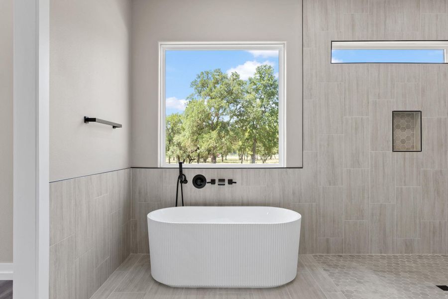 A spacious bathroom features a modern soaking tub beneath a large window, offering peaceful views of the outdoors. A spacious bathroom features a modern soaking tub beneath a large window, offering peaceful views of the outdoors.