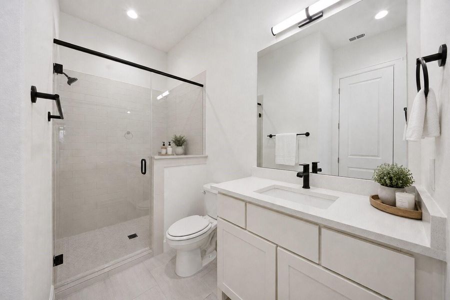 Beautifully appointed secondary bath featuring quartz countertops, frameless glass shower, matte black fixtures, and timeless modern finishes.