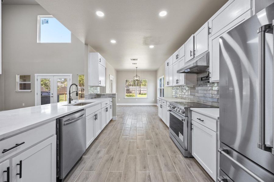 Kitchen featuring backsplash, high end appliances, white cabinets, under cabinet range hood, and a sink Kitchen featuring backsplash, high end appliances, white cabinets, under cabinet range hood, and a sink