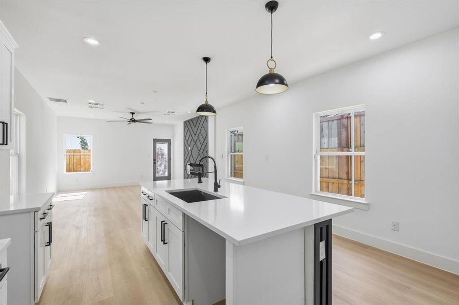 Kitchen with open floor plan, a center island with sink, light wood-type flooring, and white cabinetry