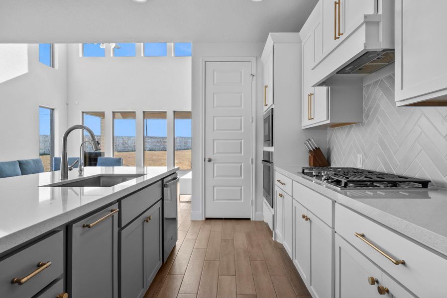 Kitchen featuring light stone counters, white cabinetry, under cabinet range hood, and light wood-style floors