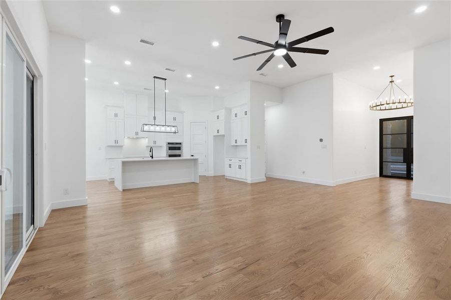 Unfurnished living room featuring hanging lights, ceiling fan, light wood finished floors, and a high ceiling