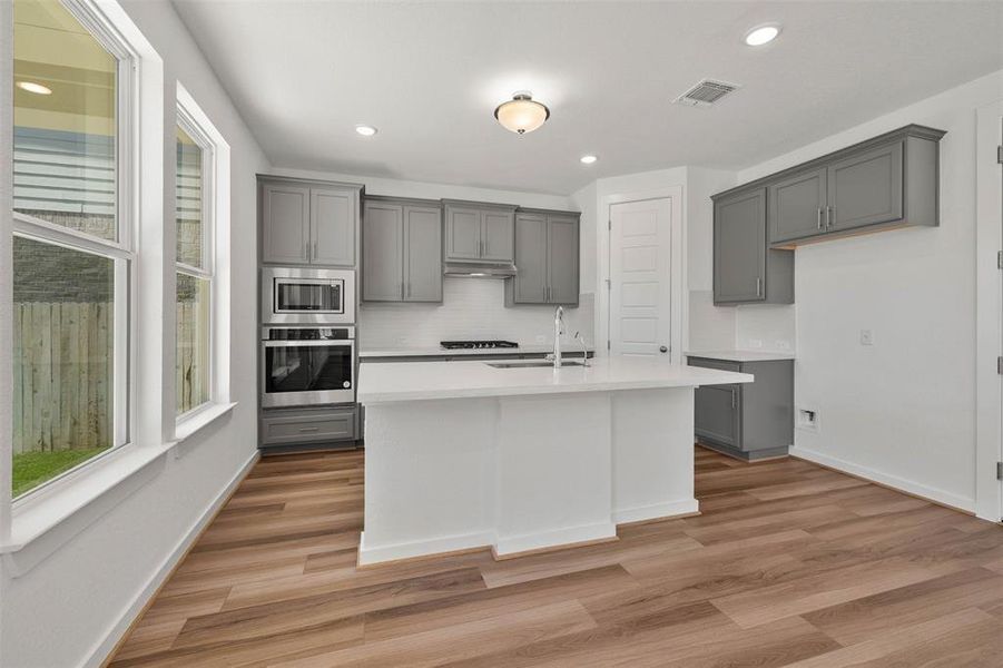 Kitchen with gray cabinetry, stainless steel appliances, recessed lighting, an island with sink, and light wood finished floors Kitchen with gray cabinetry, stainless steel appliances, recessed lighting, an island with sink, and light wood finished floors
