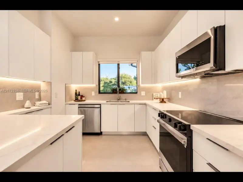 Modern kitchen with crisp white cabinetry, stone countertops, full-height stone backsplash, under-cabinet lighting, and stainless steel appliances