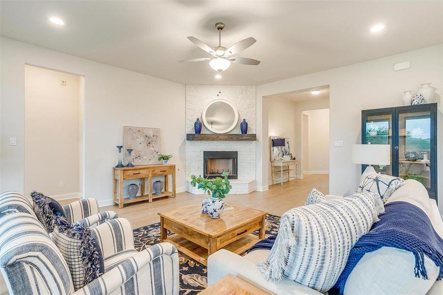 Living room with a brick fireplace, light wood-type flooring, and ceiling fan