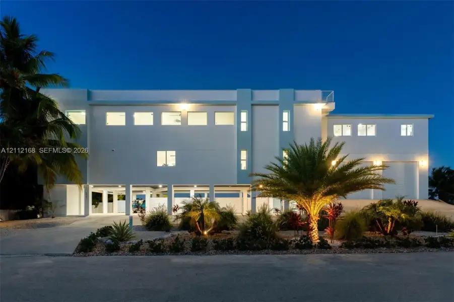 Multi-level contemporary exterior featuring a smooth stucco facade, elevated structural pilings, integrated garage bays, and a rooftop terrace Multi-level contemporary exterior featuring a smooth stucco facade, elevated structural pilings, integrated garage bays, and a rooftop terrace