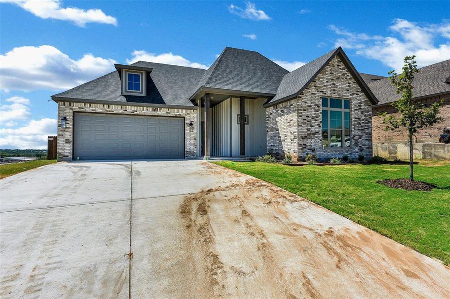 View of front of house with brick siding, roof with shingles, driveway, a front yard, and a garage
