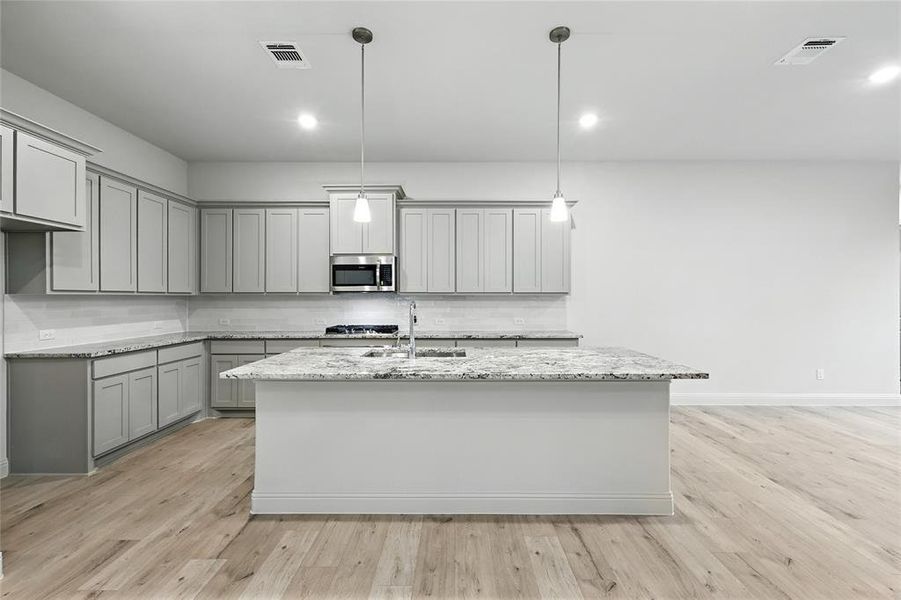 Kitchen with backsplash, gray cabinetry, light stone counters, hanging light fixtures, and light wood-style floors