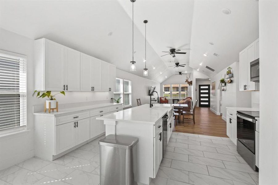 Kitchen featuring lofted ceiling, white cabinets, hanging light fixtures, appliances with stainless steel finishes, and a center island with sink