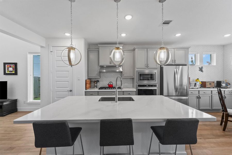 The spacious island kitchen is the heart of the home, featuring elegant quartz countertops and a stainless steel Whirlpool appliance package. The modern design and breakfast bar make this the perfect space for cooking and gathering with family.