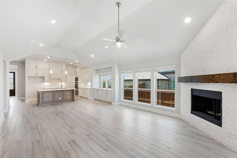 Open living area with vaulted ceiling, white brick fireplace, and kitchen with island visible in background