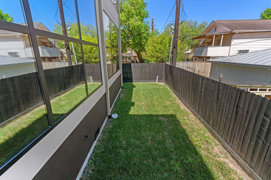The fully fenced rear yard is a private grass space enclosed on all sides, with the home's floor-to-ceiling rear glass walls looking directly into it. The indoor-outdoor connection from the main living areas is immediate and unfiltered.