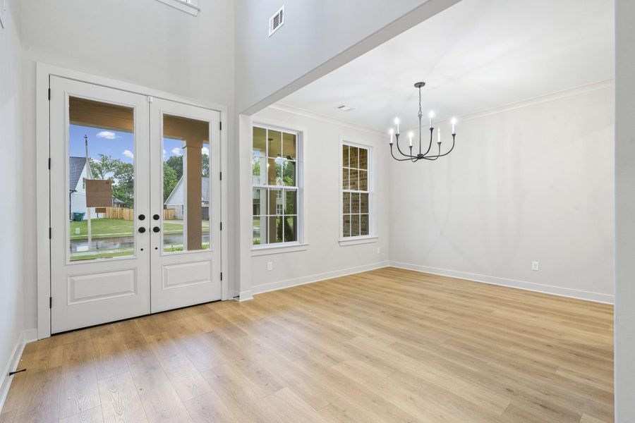 Foyer and dining area featuring light wood-finish flooring, white double-entry doors with glass panels, high ceilings, a black iron chandelier, and white trim Foyer and dining area featuring light wood-finish flooring, white double-entry doors with glass panels, high ceilings, a black iron chandelier, and white trim