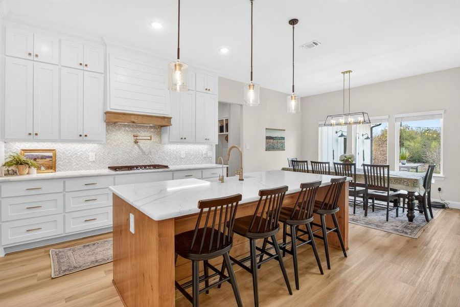 Dual tone kitchen with a kitchen breakfast bar, a kitchen island with sink, light stone counters, light wood-style flooring, and two tone cabinetry Dual tone kitchen with a kitchen breakfast bar, a kitchen island with sink, light stone counters, light wood-style flooring, and two tone cabinetry