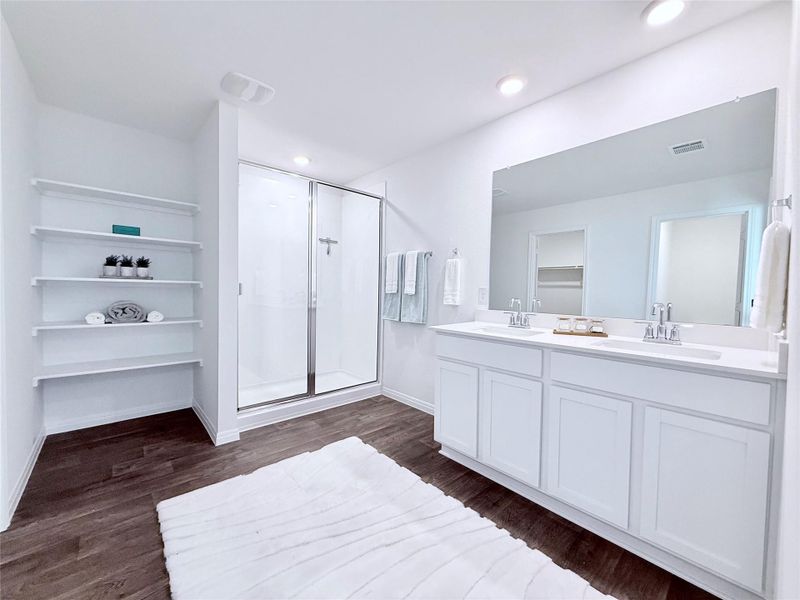 Bathroom featuring a stall shower, double vanity, a walk in closet, and dark wood-type flooring Bathroom featuring a stall shower, double vanity, a walk in closet, and dark wood-type flooring