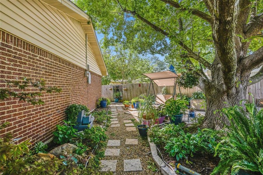 Side yard featuring a stone paver pathway, mature tree, brick exterior, and wood siding Side yard featuring a stone paver pathway, mature tree, brick exterior, and wood siding