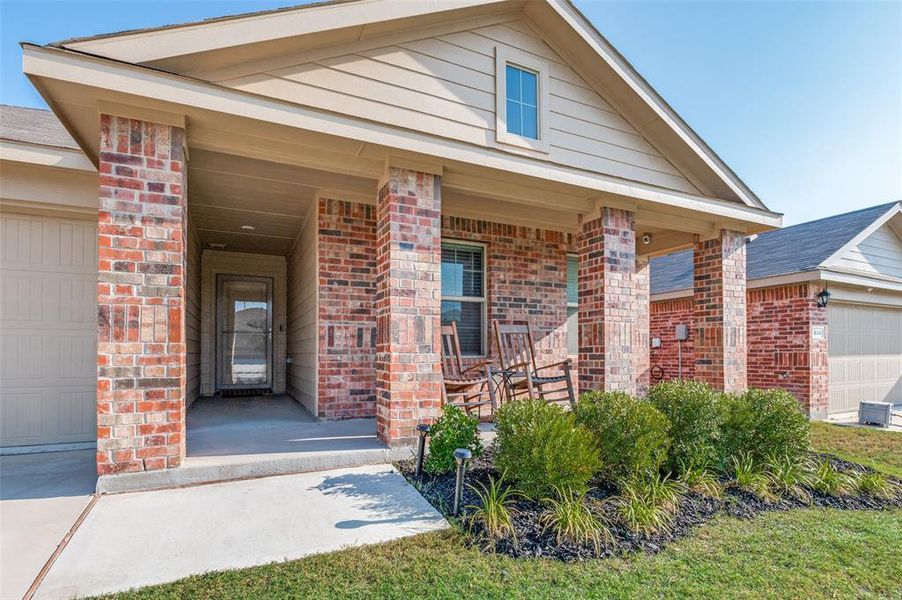 View of front of home featuring covered porch, an attached garage, and brick siding