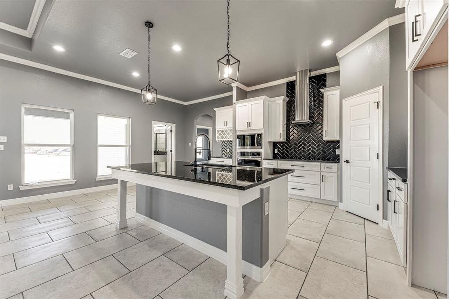 Kitchen with appliances with stainless steel finishes, a kitchen island with sink, sink, wall chimney range hood, and decorative light fixtures