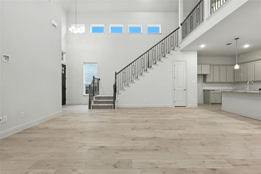 Unfurnished living room featuring stairs, light wood-type flooring, a towering ceiling, and recessed lighting