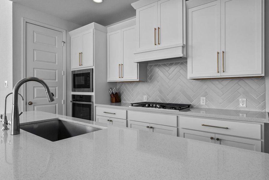 Kitchen with white cabinetry, light stone counters, stainless steel appliances, and under cabinet range hood