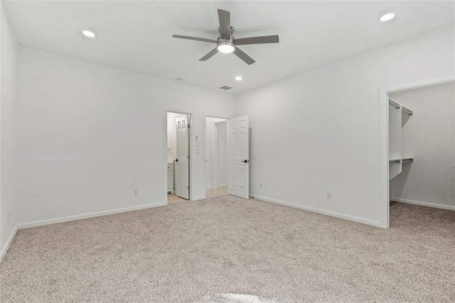 Unfurnished bedroom featuring a walk in closet, light colored carpet, recessed lighting, a ceiling fan, and connected bathroom