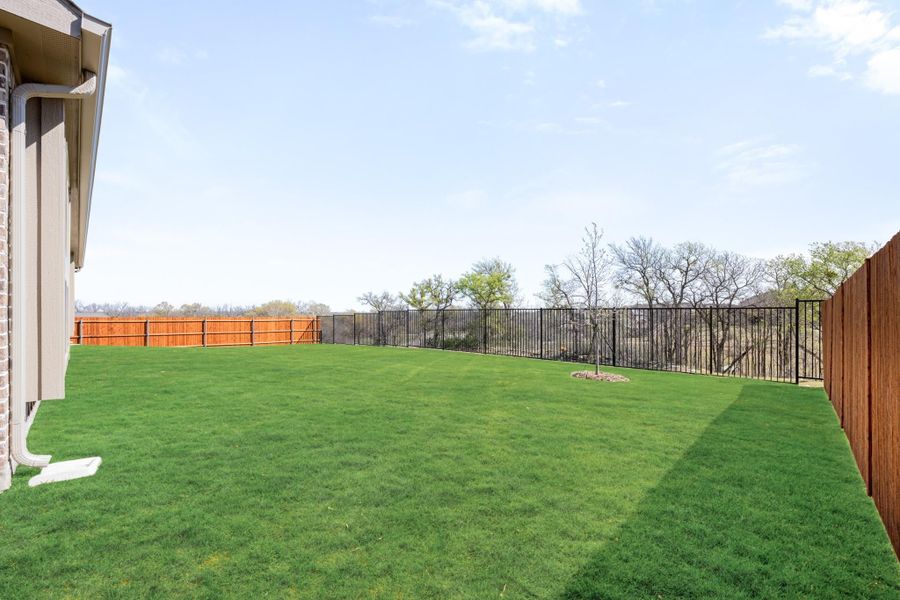 Spacious backyard with green lawn, black iron fence, and wood privacy fence panels on the sides