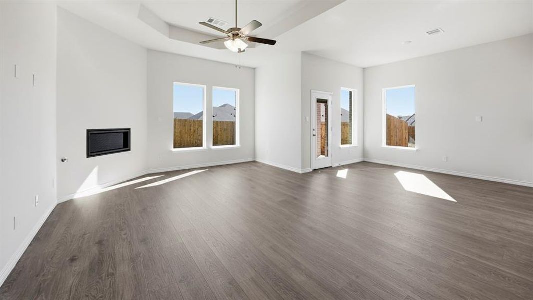 Spacious living area featuring wood-finish flooring, a contemporary ceiling fan, and recessed tray ceiling