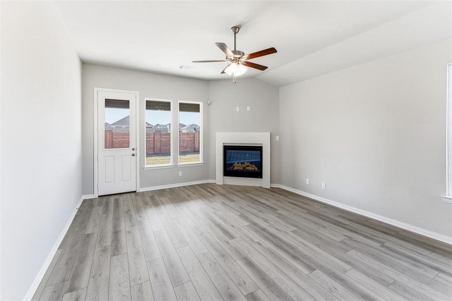 Unfurnished living room with a glass covered fireplace, light wood-type flooring, a ceiling fan, and vaulted ceiling