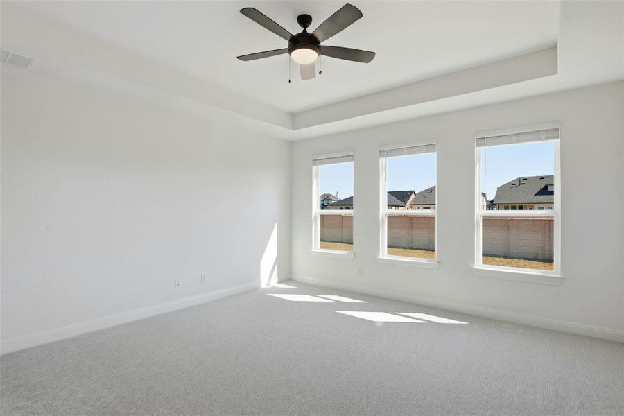 Carpeted empty room with ceiling fan and a raised ceiling